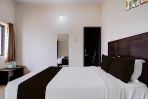 A hotel room with a bed, a bedside table, a window with curtains, and a door leading to another room.
