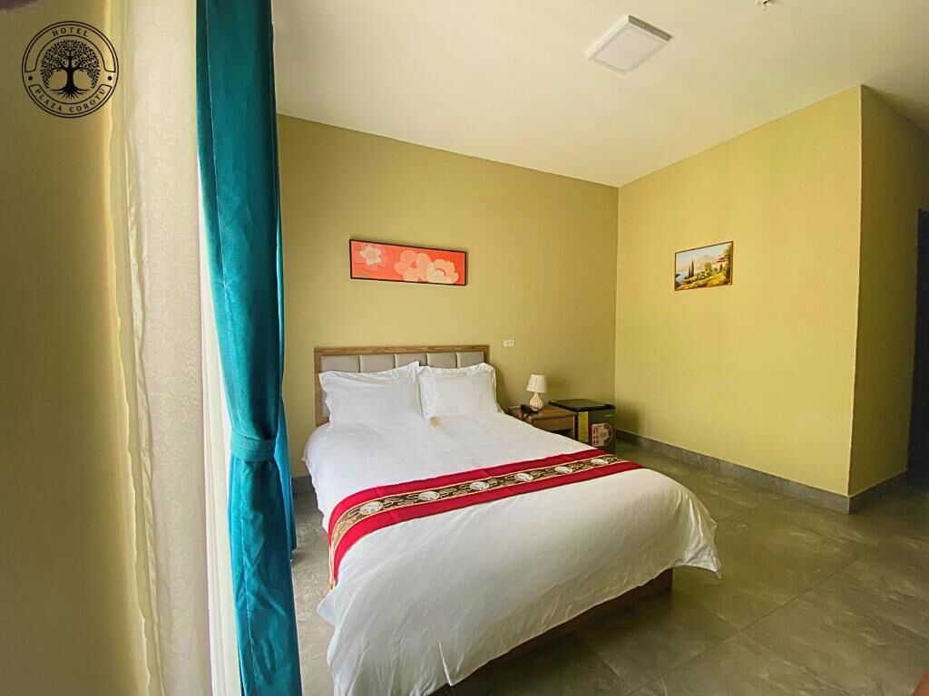A hotel room with a bed, a nightstand, a lamp, and two framed pictures on the wall.