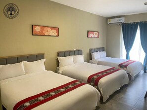 Une chambre d’hôtel avec trois lits, un climatiseur fixé au mur et deux tableaux représentant des motifs floraux.
