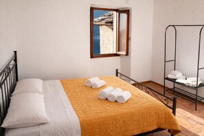 Ein Bett mit einer gelben Steude, weißen Kissen und aufgerollten Handtüchern. Über dem Bett befindet sich ein Fenster mit Blick auf eine felsige Landschaft.