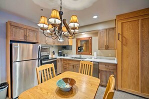 Dining area and compact kitchen with wooden cabinetry and stainless steel appliances. - Big Sky Mountain Retreat | Ski-In/Ski-Out (Big Sky)