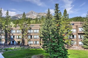 Exterior view of the multi-story lodge with tall pine trees and a mountain backdrop. - Big Sky Mountain Retreat | Ski-In/Ski-Out (Big Sky)