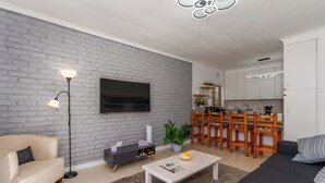 Ett vardagsrum med en soffa, ett soffbord, en tv och en matplats med stolar och ett bord.