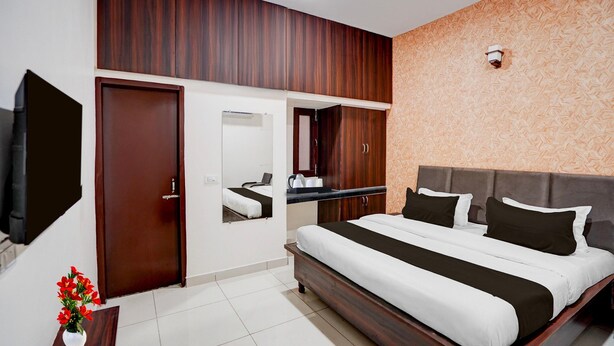 A hotel room with a large bed, a TV, a mirror, a wardrobe, and a small table with a vase.