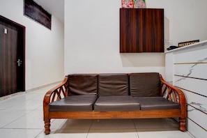 A wooden sofa with leather cushions in a room with white walls, a reception desk, and a door. - Classic Hotel Charanjit Arora (Ludhiana)
