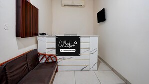 A reception area with a marble counter, a sofa, a TV mounted on the wall, and an air conditioning unit.