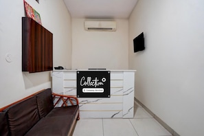 A reception area with a marble counter, a sofa, a TV mounted on the wall, and an air conditioning unit. - Classic Hotel Charanjit Arora (Ludhiana)