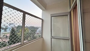 A corner of a room with a mesh window, a closed door, and a view of buildings and trees outside. - Beautiful 1-bedroom hotel with AC in peaceful Rishikesh (Rishikesh)