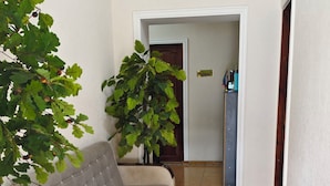 A narrow hallway with a grey sofa, two potted plants, and a door leading to a room. - Tashkent Atlas  (Tashkent)