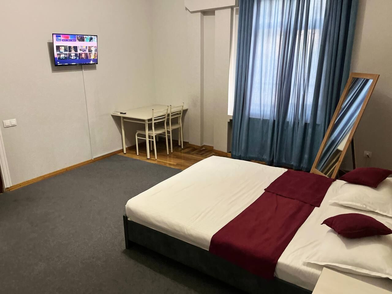 Una habitación de hotel con cama, escritorio, silla, televisor y espejo.