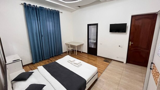 A hotel room with a bed, a desk, a chair, a TV, and a bathroom door. - Tashkent Atlas  (Tashkent)