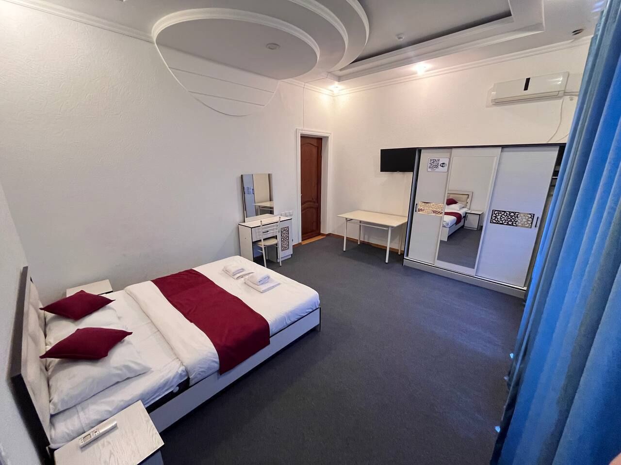 A hotel room with a bed, a desk, a chair, a mirror, and a wardrobe.