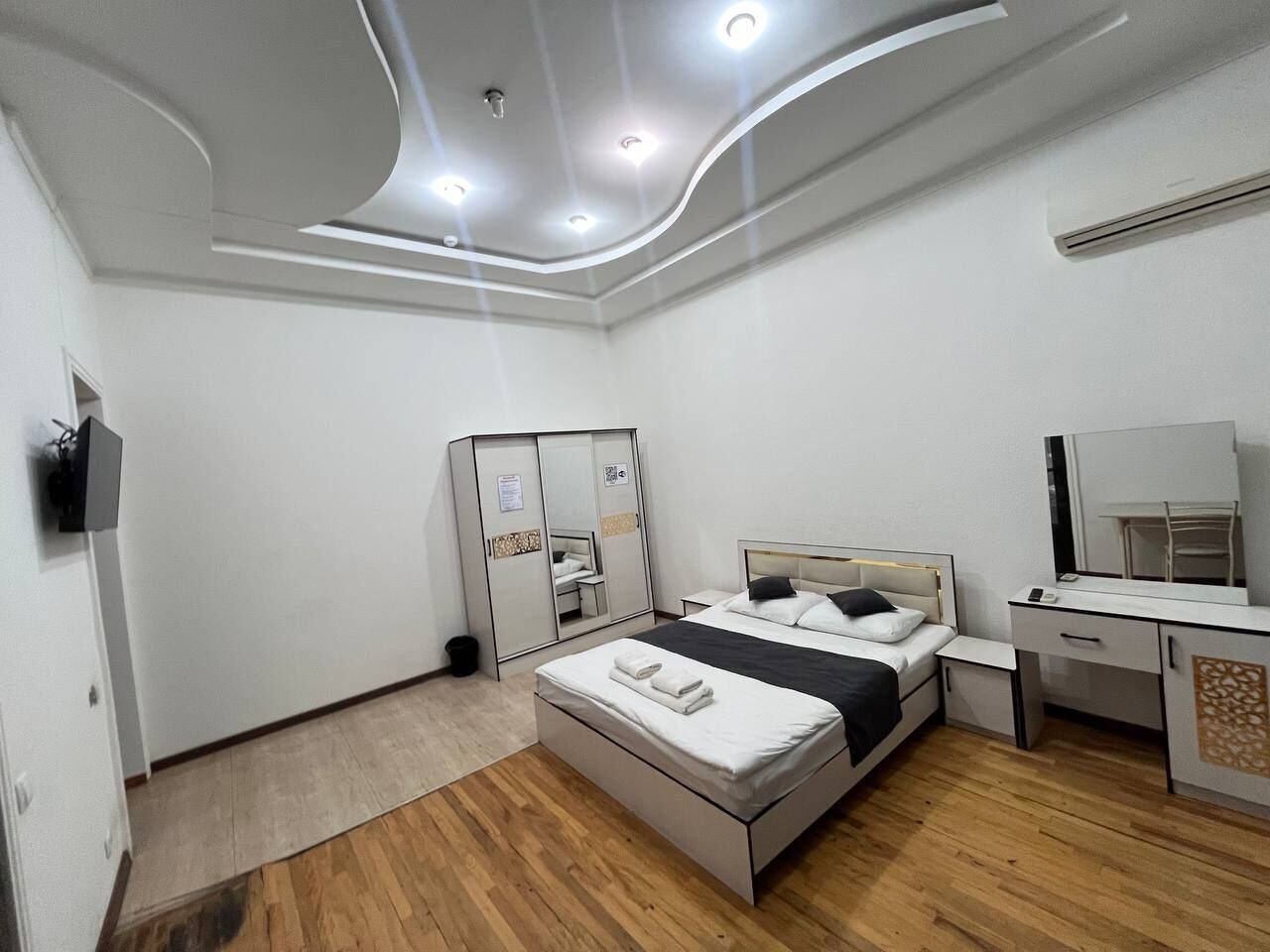 A modern hotel room with a bed, bedside table, wardrobe, and a mirror.