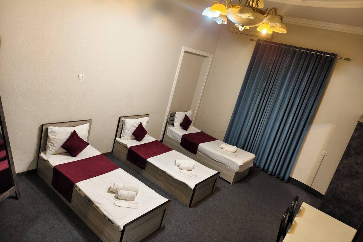 A hotel room with three single beds, a wooden headboard, a large mirror, and a chandelier.