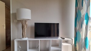 A modern living room with a flat-screen TV on a white stand, a lamp, and a remote control. - T2 APARTMENT ON 1ST FLOOR 200 M FROM GRANDE PLAGE AND SHOPS (Saint-Cast-le-Guildo)