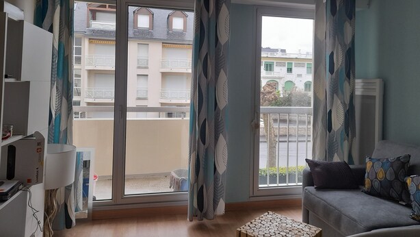 A living room with a sofa, a small table, and a window with curtains. - T2 APARTMENT ON 1ST FLOOR 200 M FROM GRANDE PLAGE AND SHOPS (Saint-Cast-le-Guildo)