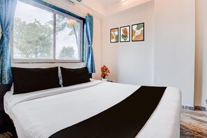 A neatly made bed with white and black bedding, a window with blue curtains, and three framed artworks on the wall.