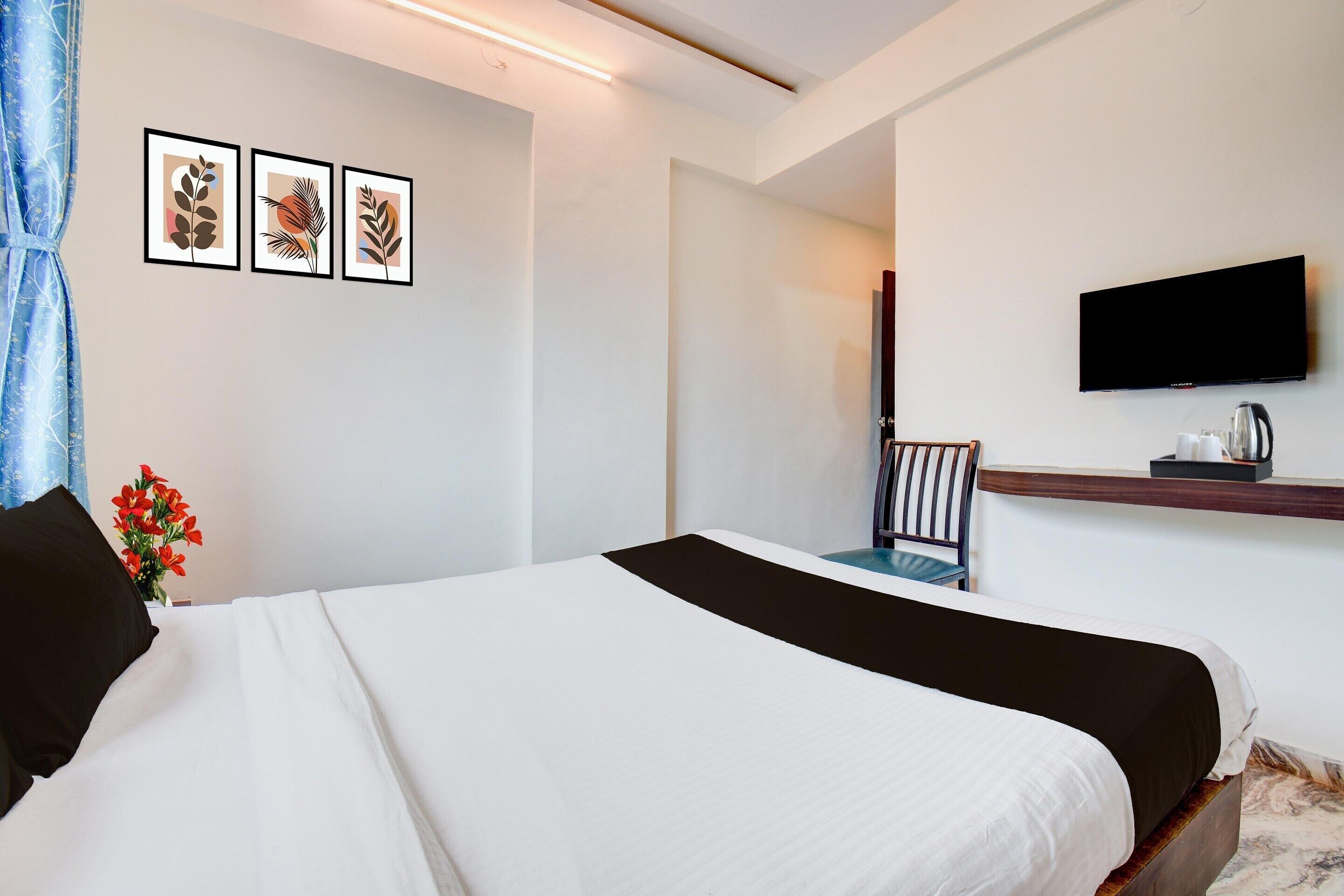 Een hotelkamer met een bed, een aan de muur bevestigde televisie, een klein tafeltje met een waterkoker en een stoel.