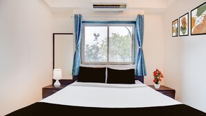 Hotelkamer met een groot bed, nachtkastje met lamp, raam met gordijnen en lijstwerken aan de muur.