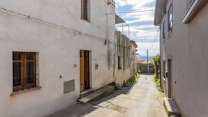 Une rue étroite, bordée de bâtiments des deux côtés, avec une porte bien visible et un ciel dégagé.