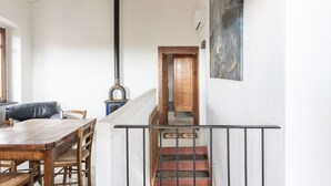 Un coin repas avec une table et des chaises en bois, un poêle noir, un escalier et un tableau accroché au mur.