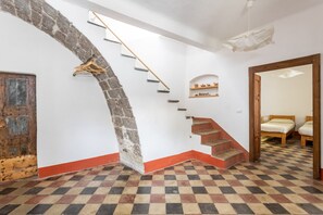 Eine Treppe mit steinernen Bögen, einer Holztür, einem Schachbrettfußboden und einem Spiegel, der ein Bett widerspiegelt.