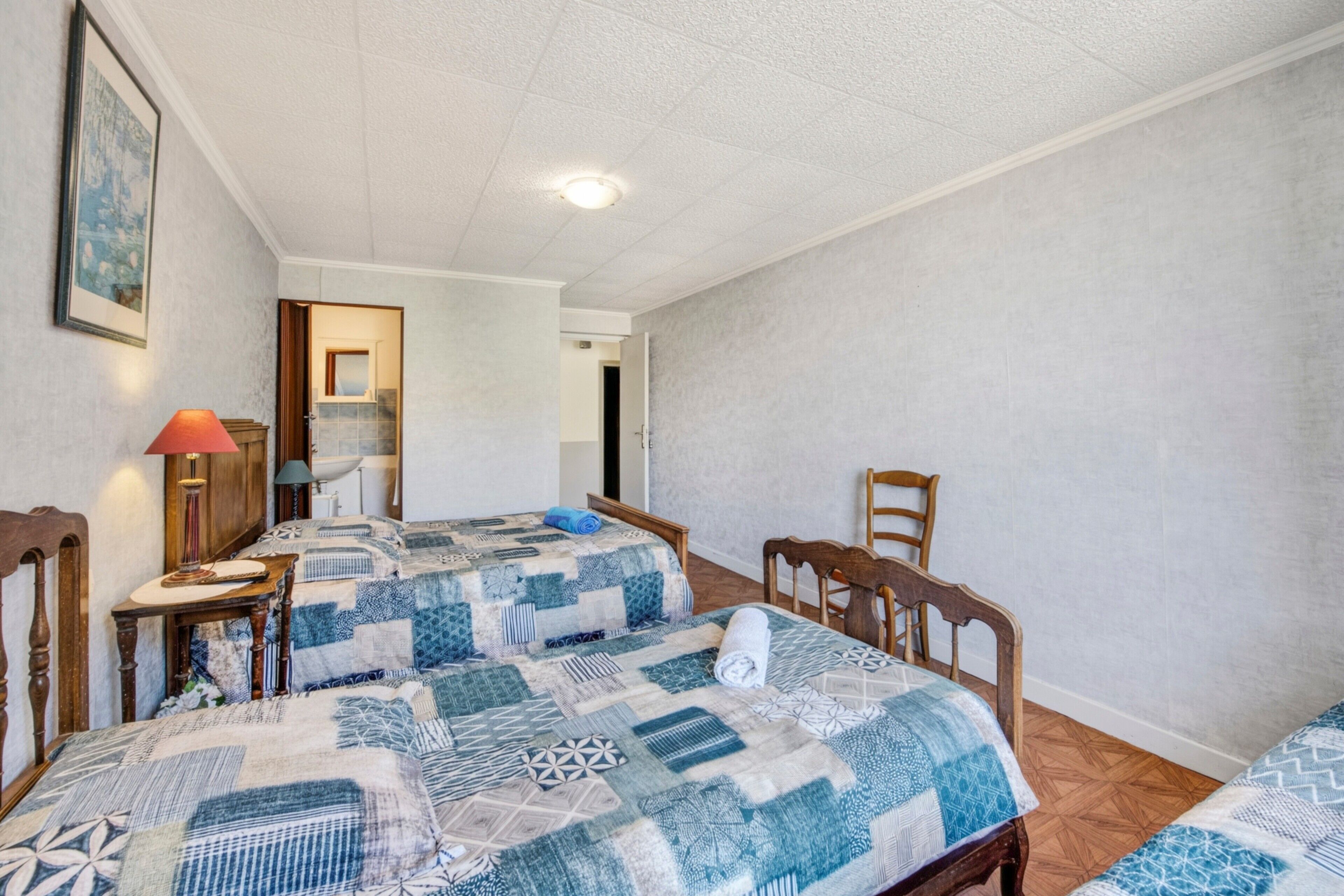 Una habitación con dos camas, una silla de madera, una mesa y una lámpara.