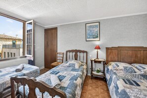 Une chambre avec deux lits, une tête de lit en bois, une fenêtre, un tableau et une lampe.