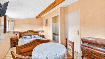 A bedroom with a wooden bed, a round table with a white tablecloth, a dresser with drawers, and a door.