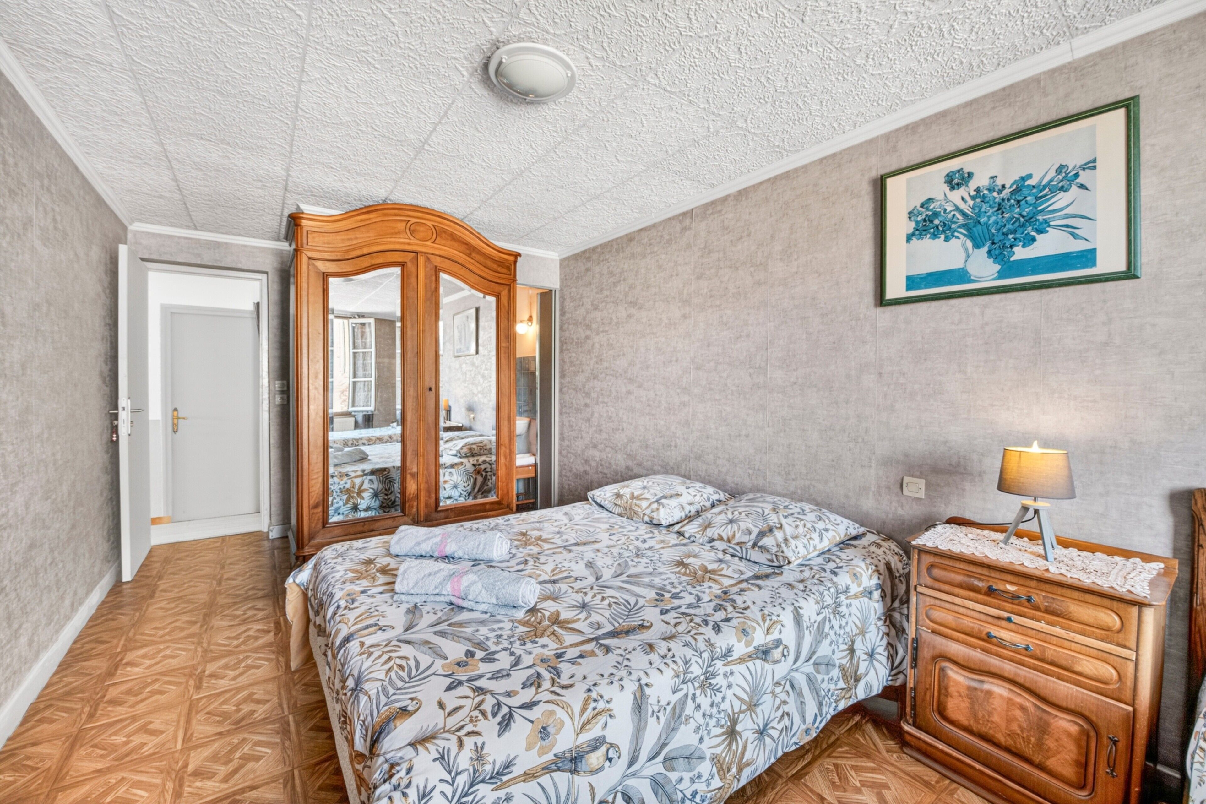 A bedroom with a bed, a wooden dresser, a mirror, and a framed picture on the wall.