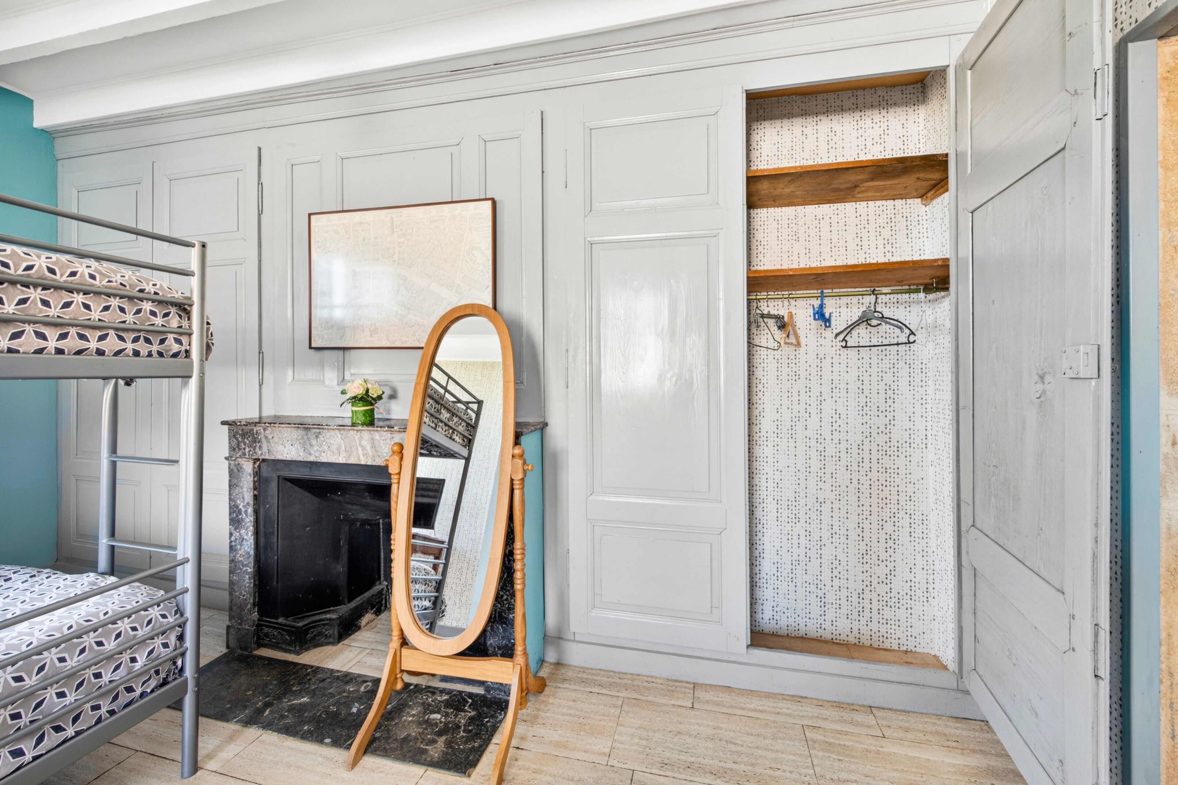 Een kamer met een stapelbed, een open haard, een spiegel en een garderobe met planken.