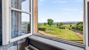 Une fenêtre donnant sur un paysage rural, avec des champs, des arbres et une colline au loin.