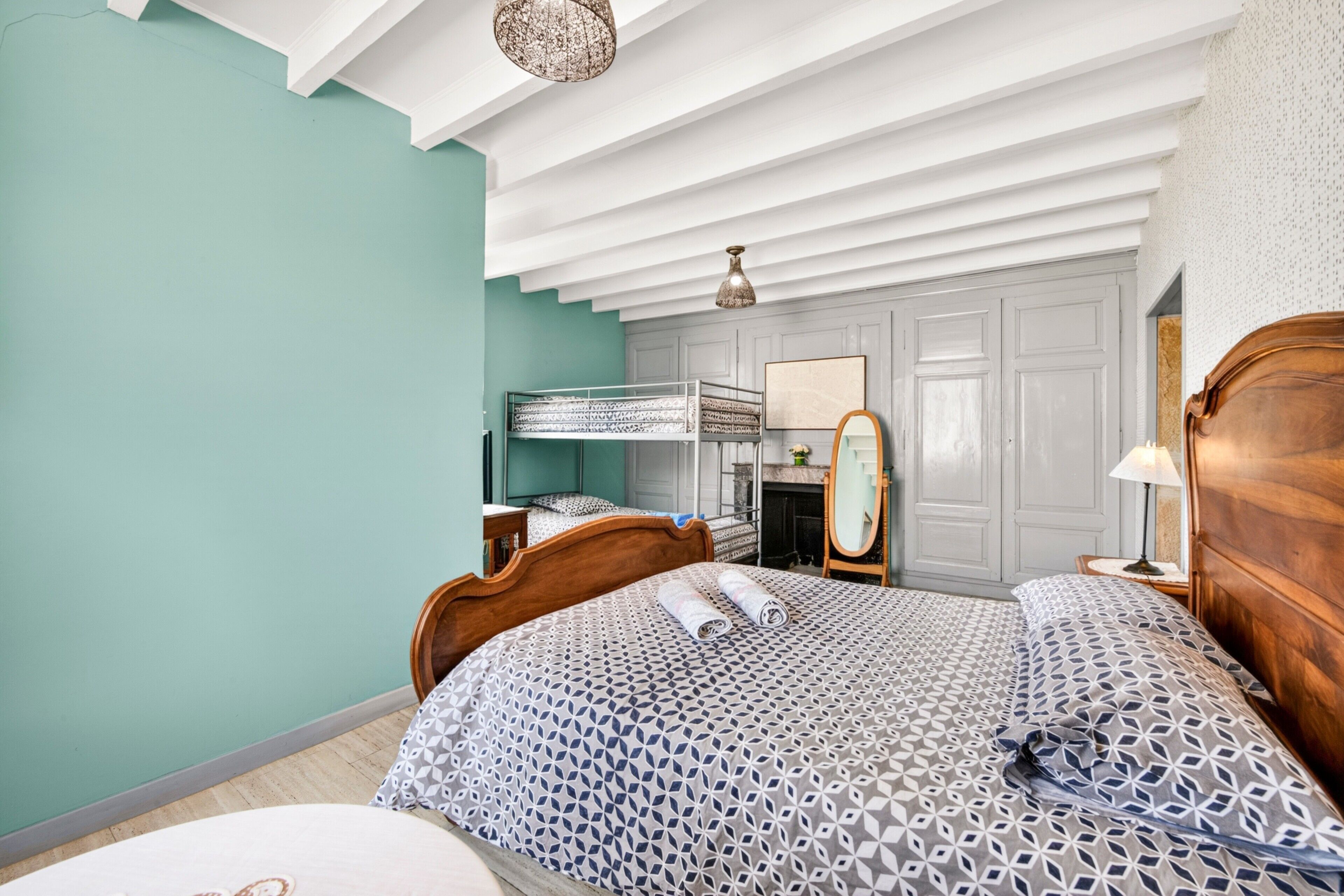 Een slaapkamer met een stapelbed, een houten hoofdbord, een nachtkastje met een lamp en een spiegel.