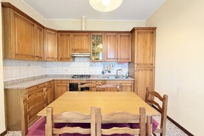 Una cucina con mobili in legno, un piano di lavoro in granito, un fornello e un tavolo da pranzo con sedie.