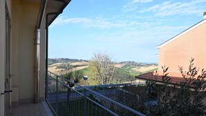 A balcony with a metal railing, a tiled floor, and a view of a hilly landscape. - SE235 - Senigallia, large three-room apartment with furnished courtyard (Roncitelli)