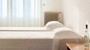 A hotel room with two beds, a wooden nightstand, a bottle of water, and a radiator. - SE235 - Senigallia, large three-room apartment with furnished courtyard (Roncitelli)
