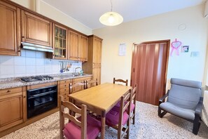 A kitchen with wooden cabinets, a granite countertop, a dining table with chairs, and a gray armchair. - SE235 - Senigallia, large three-room apartment with furnished courtyard (Roncitelli)