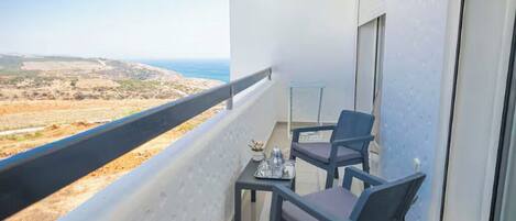Un balcón con mesa y sillas, una mesita con bandeja y vistas a la costa.