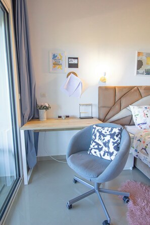 A modern bedroom with a desk, a comfortable chair, a bed, and a window with curtains.