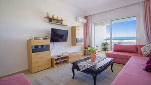 Una sala de estar con televisor, muebles de madera, un sofá y vista al mar.