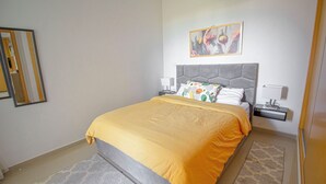 Un dormitorio con una cama, mesitas de noche, una lámpara, un cuadro y una alfombra estampada.