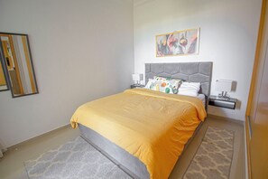 A bedroom with a bed, nightstands, a lamp, a painting, and a patterned rug. - Panoramic Resort Apartment • Sea, Lake & Golf Views • Pools & Tennis (Asilah)