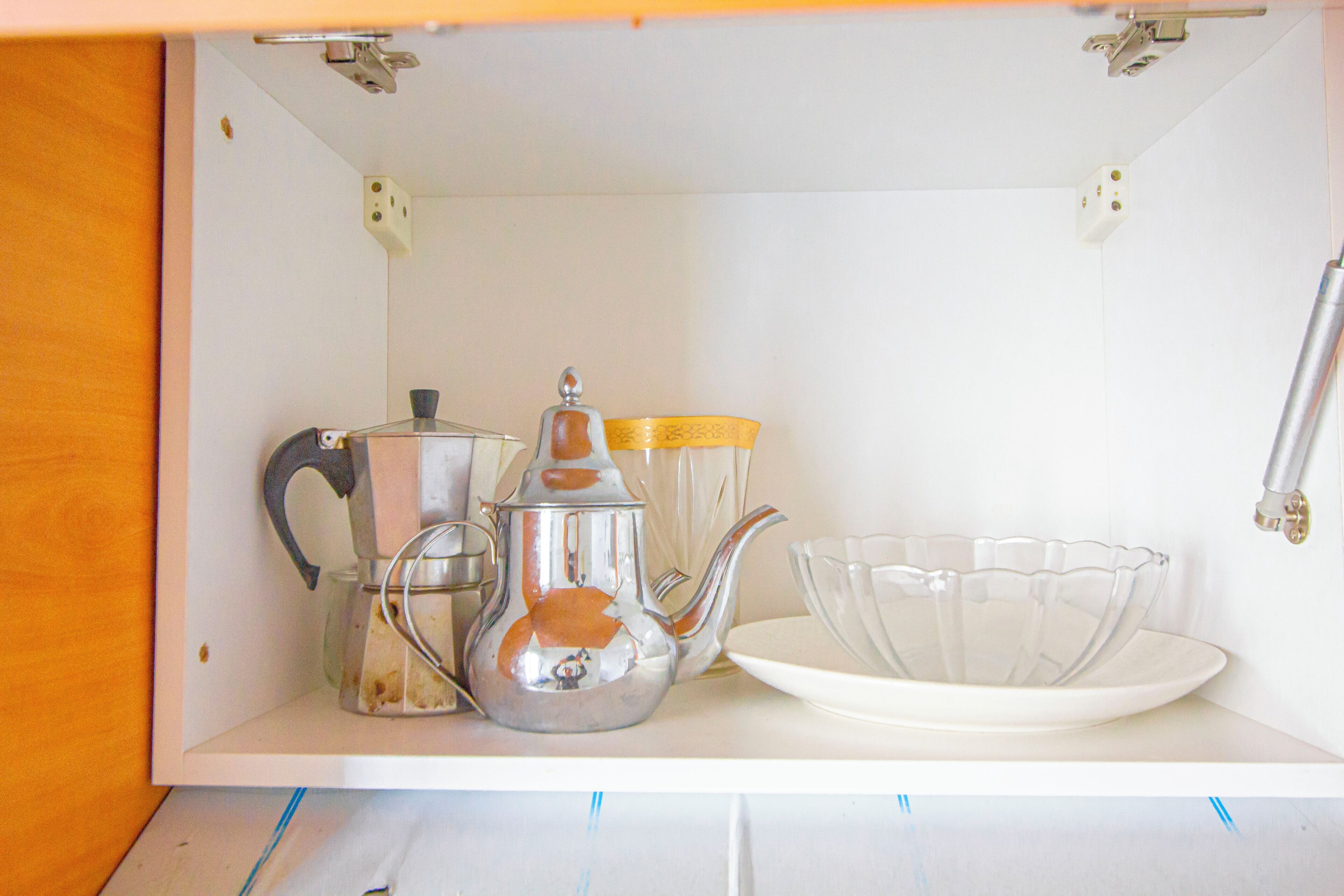 A kitchen cabinet with a tea kettle, a glass container, and a clear glass bowl.