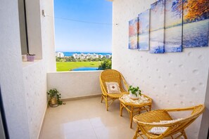 A balcony with wicker furniture, a view of a golf course, and a cityscape. - Panoramic Resort Apartment • Sea, Lake & Golf Views • Pools & Tennis (Asilah)