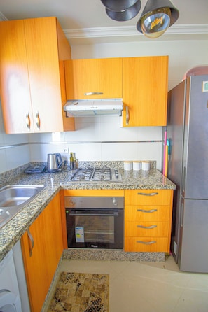 A kitchen with wooden cabinets, a stainless steel refrigerator, a built-in oven, and a granite countertop.