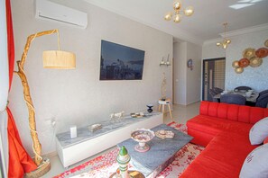 A living room with a sofa, a coffee table, a lamp, a painting, and a dining area.