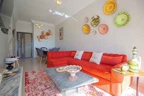 A living room with a red sofa, a marble coffee table, and a dining area with a chair and table.