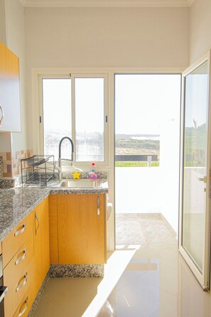 A modern kitchen with granite countertops, wooden cabinets, and a large window offering a view of the outdoors.