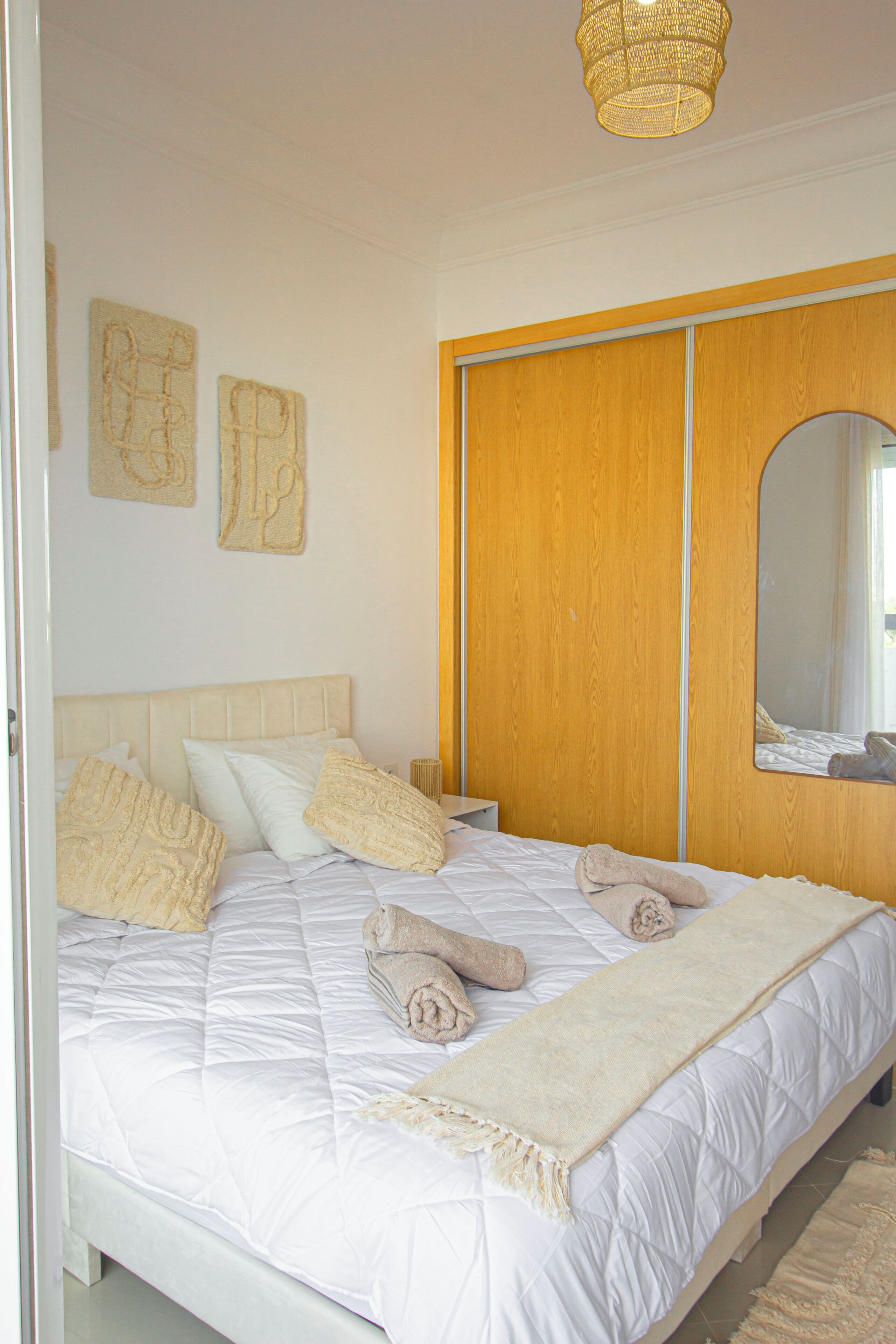 Une chambre à coucher avec un lit, des oreillers, une couverture, une armoire en bois et un miroir.