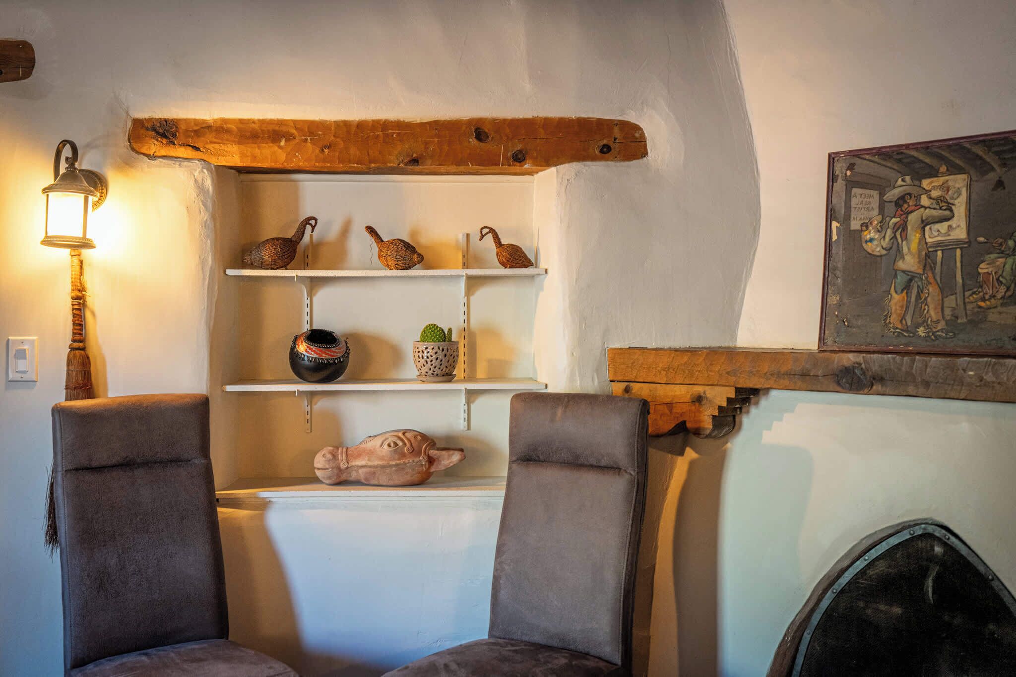 A cozy room with a fireplace, two armchairs, shelves with decorative items, and a wall-mounted lamp.